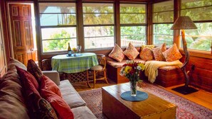 A cozy room with a sofa, a wooden coffee table with a vase, a dining table with a green tablecloth, and a bench with patterned cushions. - Gulfside 1Br/1Ba Captain's Quarters On Anna Maria Island (Holmes Beach)