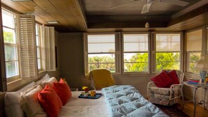 A bedroom with a bed, a chair, a table, and a window with a view of greenery. - Gulfside 1Br/1Ba Captain's Quarters On Anna Maria Island (Holmes Beach)