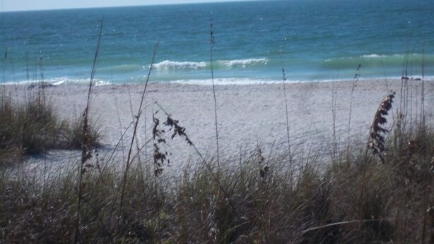 A beach with sand and grass in the foreground, and a calm sea in the background. - Gulfside 1Br/1Ba Captain's Quarters On Anna Maria Island (Holmes Beach)