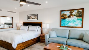 A bedroom with a bed, a sofa, a coffee table, and a painting of a beach scene.