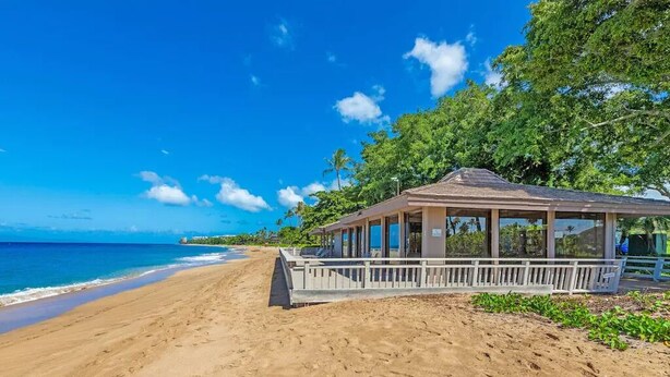 A beachside building with a covered porch, adjacent to a sandy beach and the ocean.