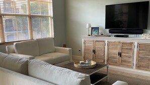 Un salon avec un canapé blanc, une table basse et un téléviseur posé sur un meuble.