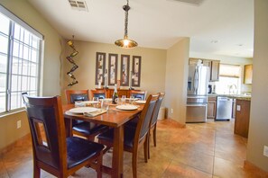 A dining area with a wooden table set for four, surrounded by chairs, and a kitchen in the background.