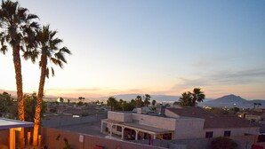 Una piscina con sdraio, palme e vista sulla città al tramonto.