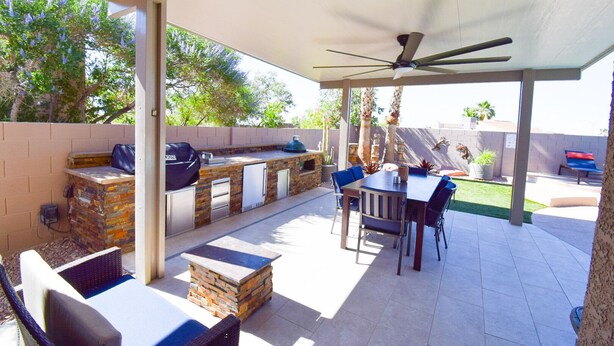 Patio esterno con barbecue in pietra, posti a sedere e ventola a soffitto.