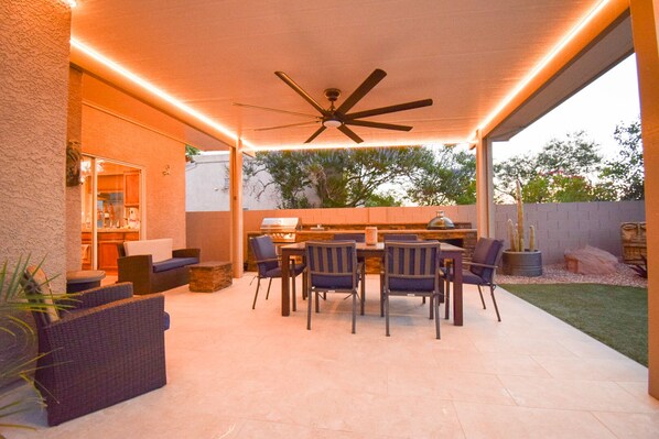An outdoor patio with a ceiling fan, a barbecue grill, and a dining area with chairs and a table.