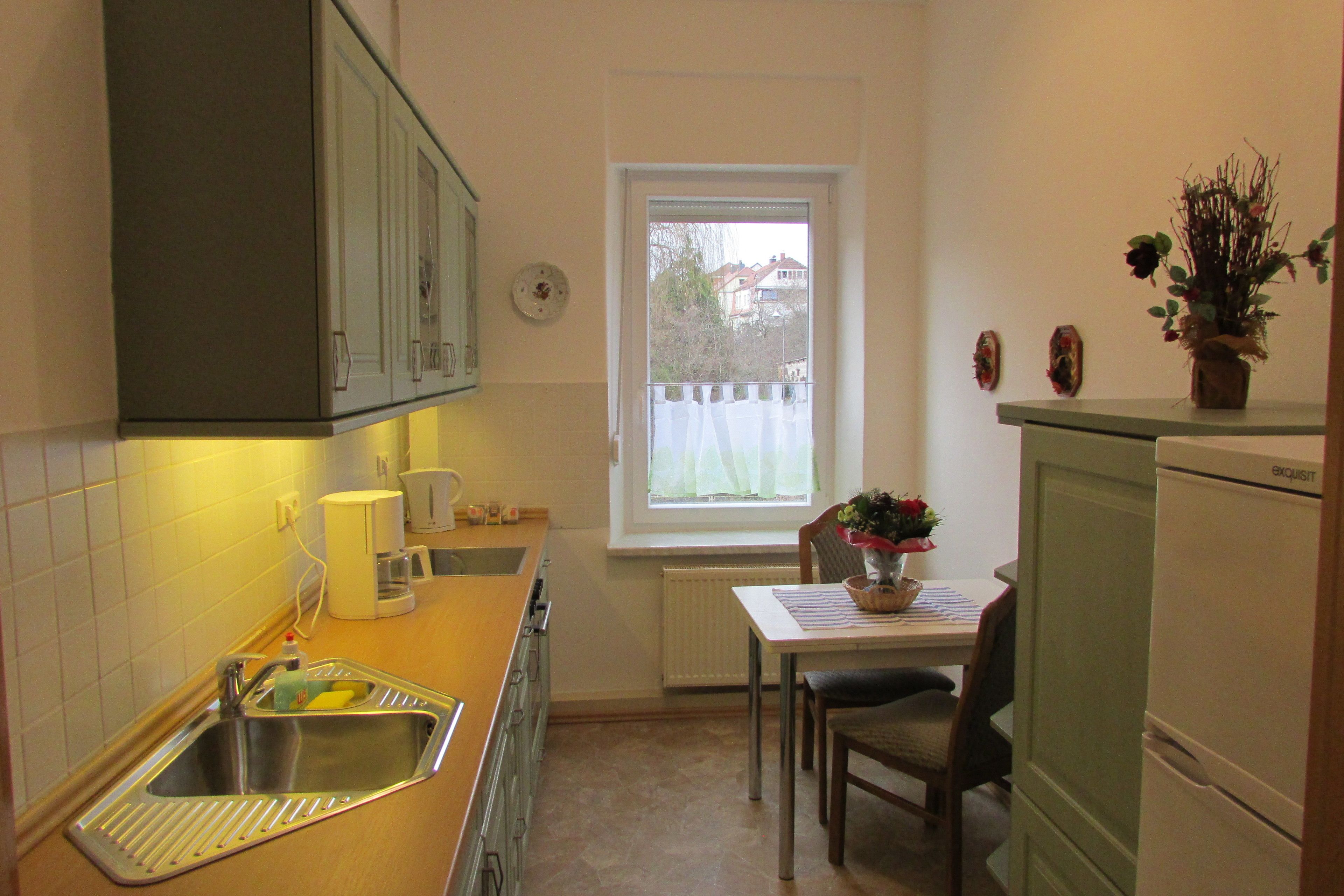 A compact kitchen with a sink, a window, a dining table with chairs, and a refrigerator.