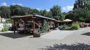 A covered parking area with a car and a building in the background. - NoOaks (Meissen)