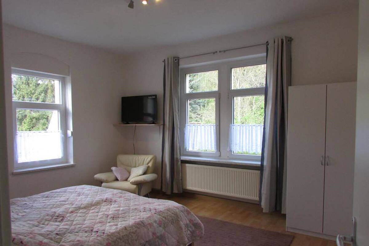 Une chambre avec un lit, une chaise, une armoire et un téléviseur fixé au mur.