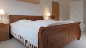 A bedroom with a wooden bed, nightstands, a wardrobe, and a painting on the wall. - NoOaks (Meissen)