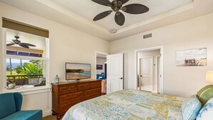 A bedroom with a bed, a dresser, a TV, a ceiling fan, and a window with a view of the outdoors.