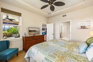 A bedroom with a bed, a dresser, a TV, a ceiling fan, and a window with a view of the outdoors.