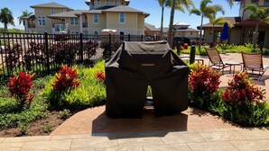A patio area with a grill cover, surrounded by landscaped plants and a fence. - Luxury condo with central A/C and golf and ocean views (Koloa)
