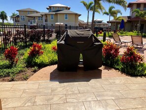 A patio area with a grill cover, surrounded by landscaped plants and a fence. - Luxury condo with central A/C and golf and ocean views (Koloa)