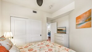 A bedroom with a bed, a dresser, a television, and a painting on the wall. - Luxury condo with central A/C and golf and ocean views (Koloa)