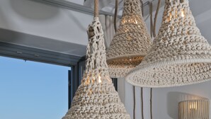 A dining area with a view of the sea, featuring a table and chairs, and a hanging crochet light fixture. - Villa Moonflower (Mykonos)