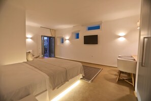 A modern bedroom with a bed, bedside tables, a flat-screen TV, and a seating area with chairs. - Villa Moonflower (Mykonos)