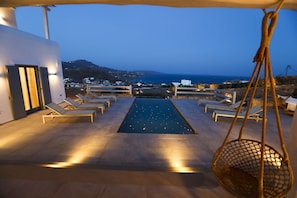 A pool area with lounge chairs and a hanging basket, overlooking a coastal landscape. - Villa Moonflower (Mykonos)
