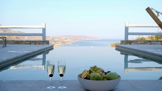 A table with two glasses of champagne, a bowl of fruit, and a view of the sea. - Villa Moonflower (Mykonos)