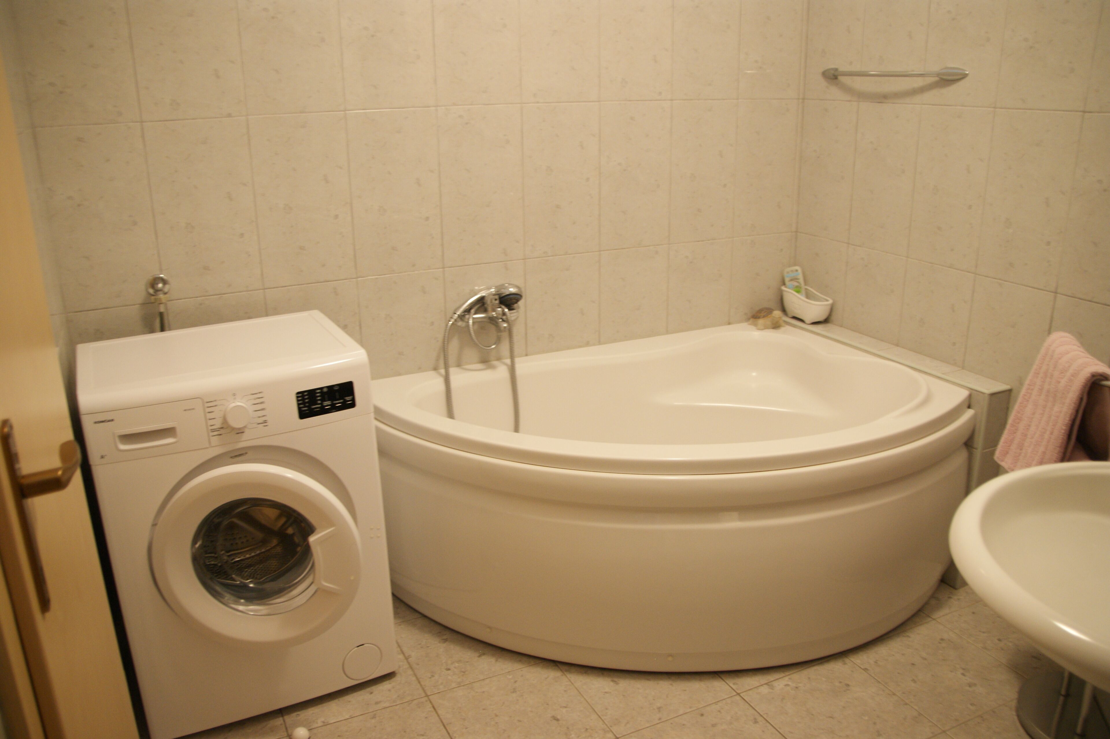 A compact bathroom with a washing machine, a bathtub, and a sink.