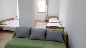 Ein Zimmer mit zwei Einzelbetten, einem grünen Sofa und einem kleinen Tisch mit einer Lampe.