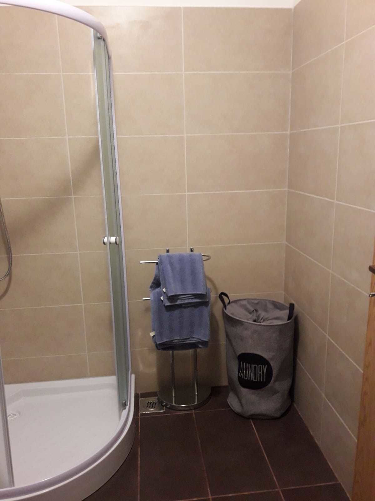 Een badkamer met een glazen douchecabine, een handdoekrek met opgevouwen handdoeken, en een waszak met de tekst 'Laundry'.