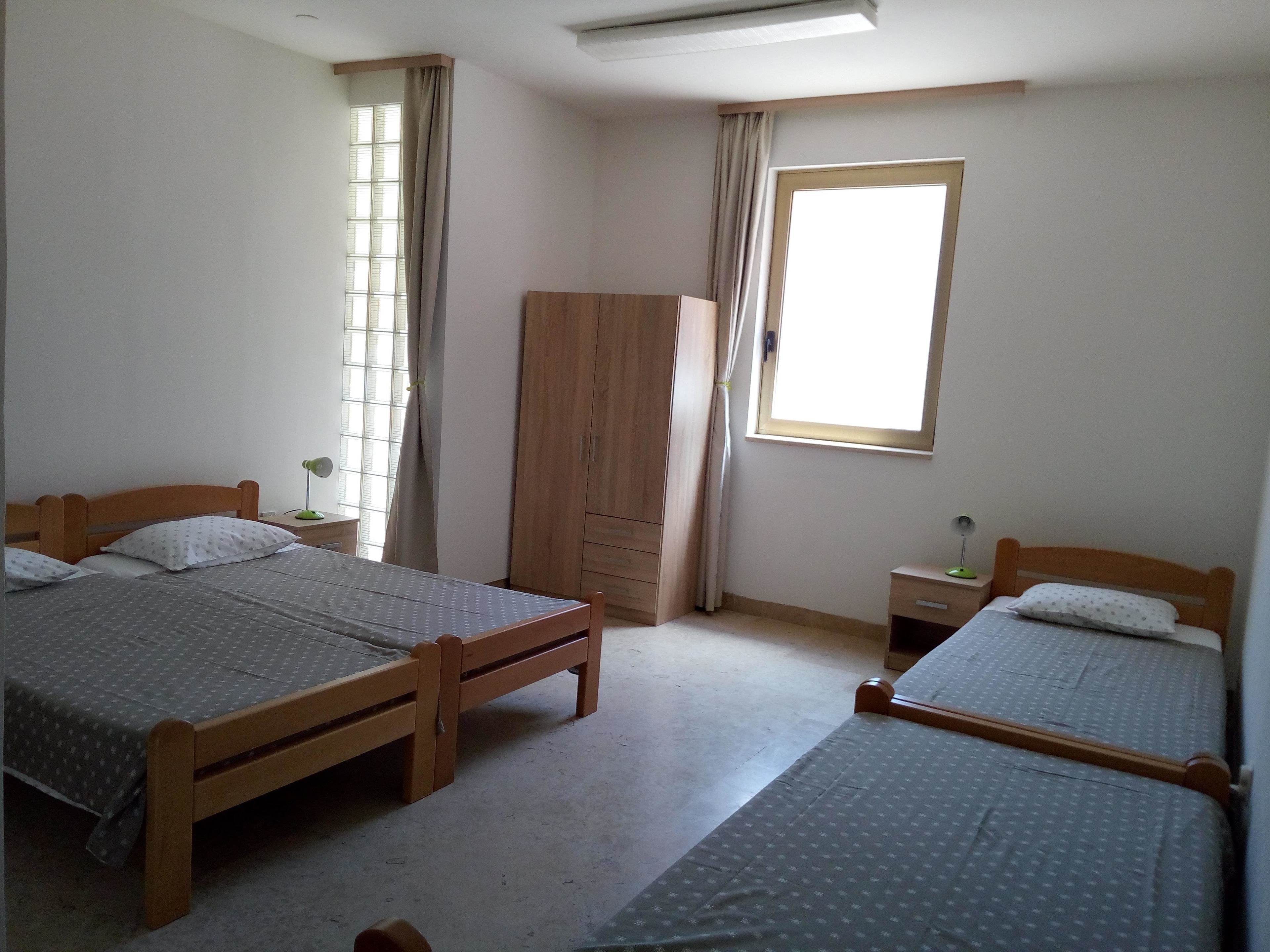 A bedroom with two wooden beds, a wardrobe, a window, and a nightstand.