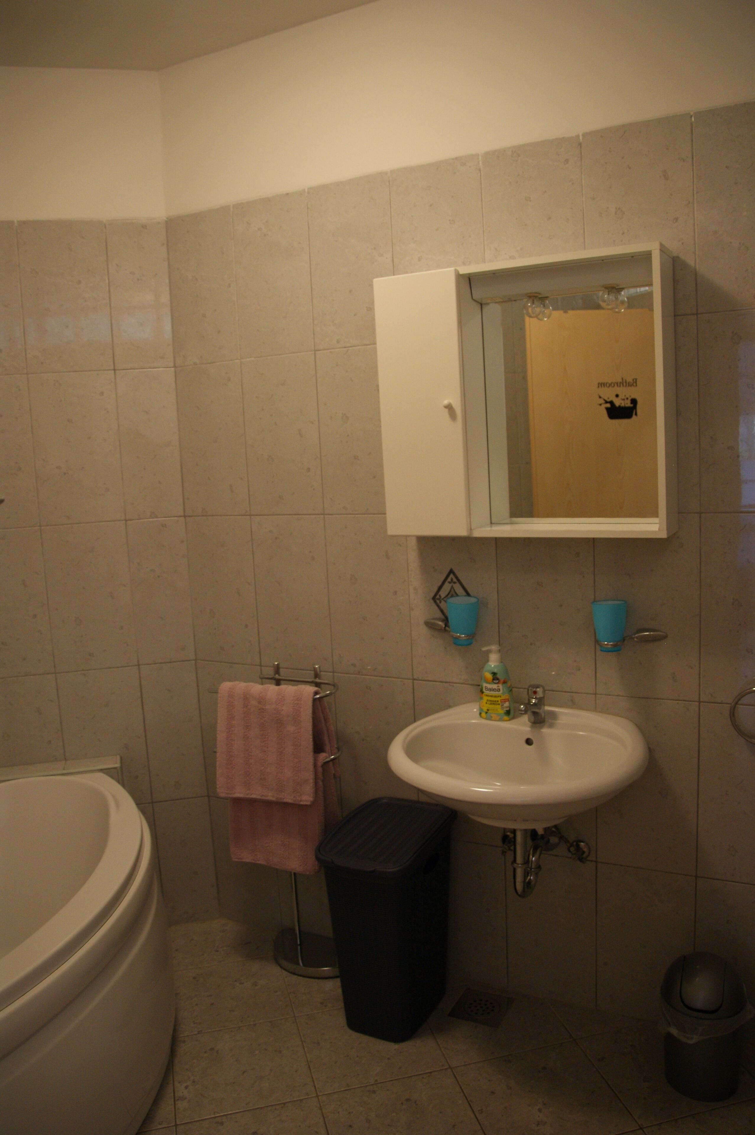 Un baño con bañera, lavamanos, espejo y dos tazas azules en la pared.