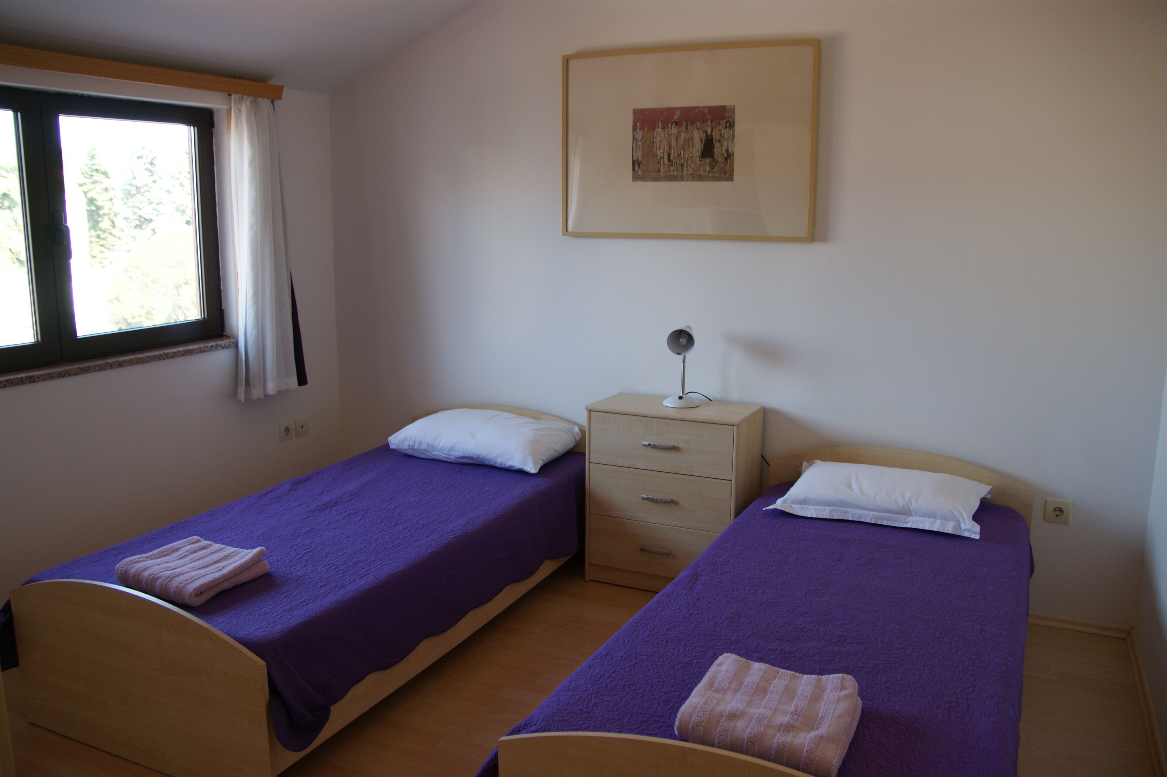 A bedroom with two single beds, a nightstand, a lamp, and a framed picture on the wall.