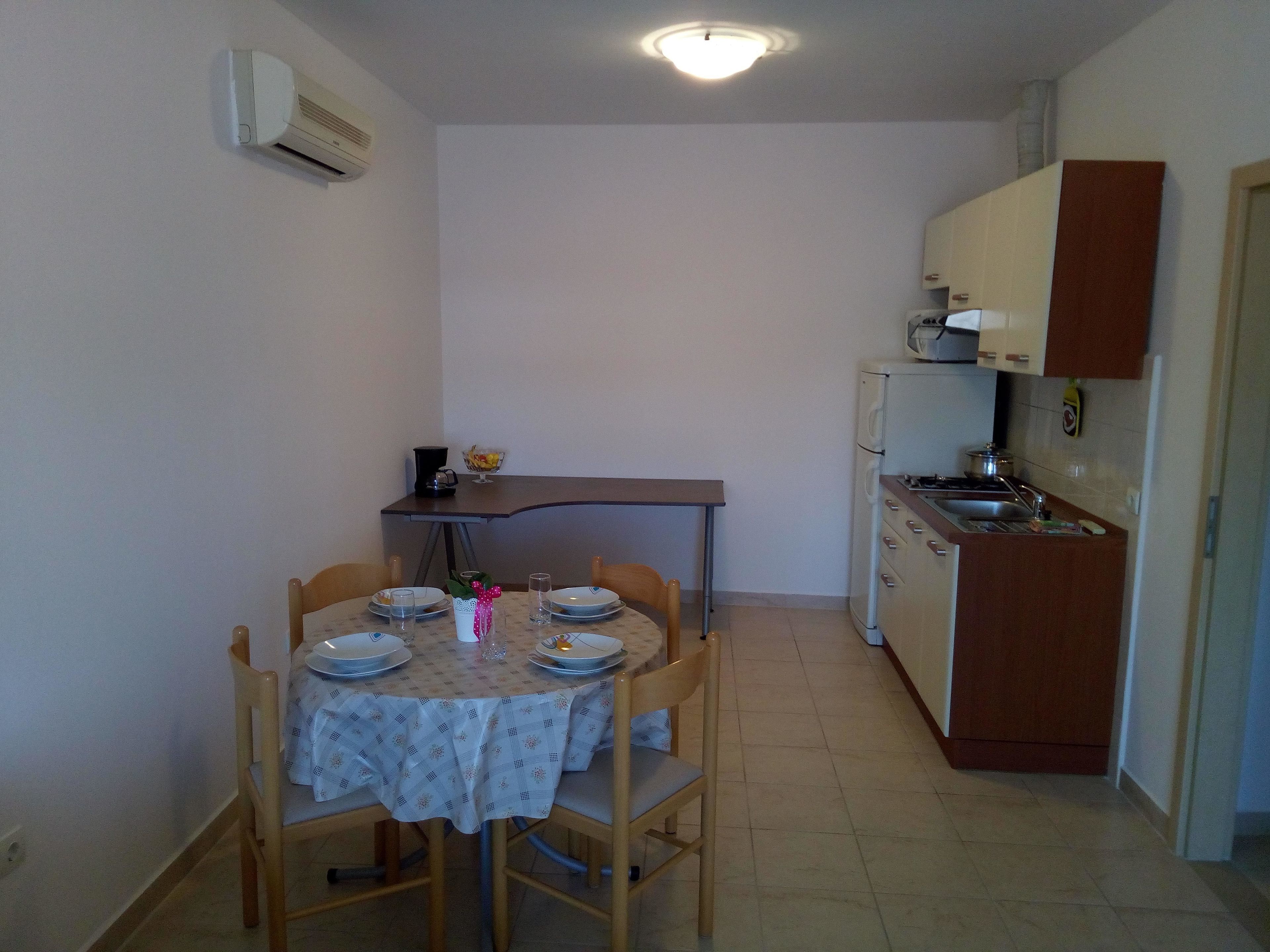 A compact kitchen with a dining table set for two, a small refrigerator, and a microwave.