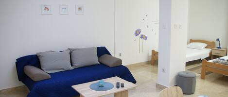 A room with a blue sofa, a small table with a remote control, and a bed with a wooden headboard.