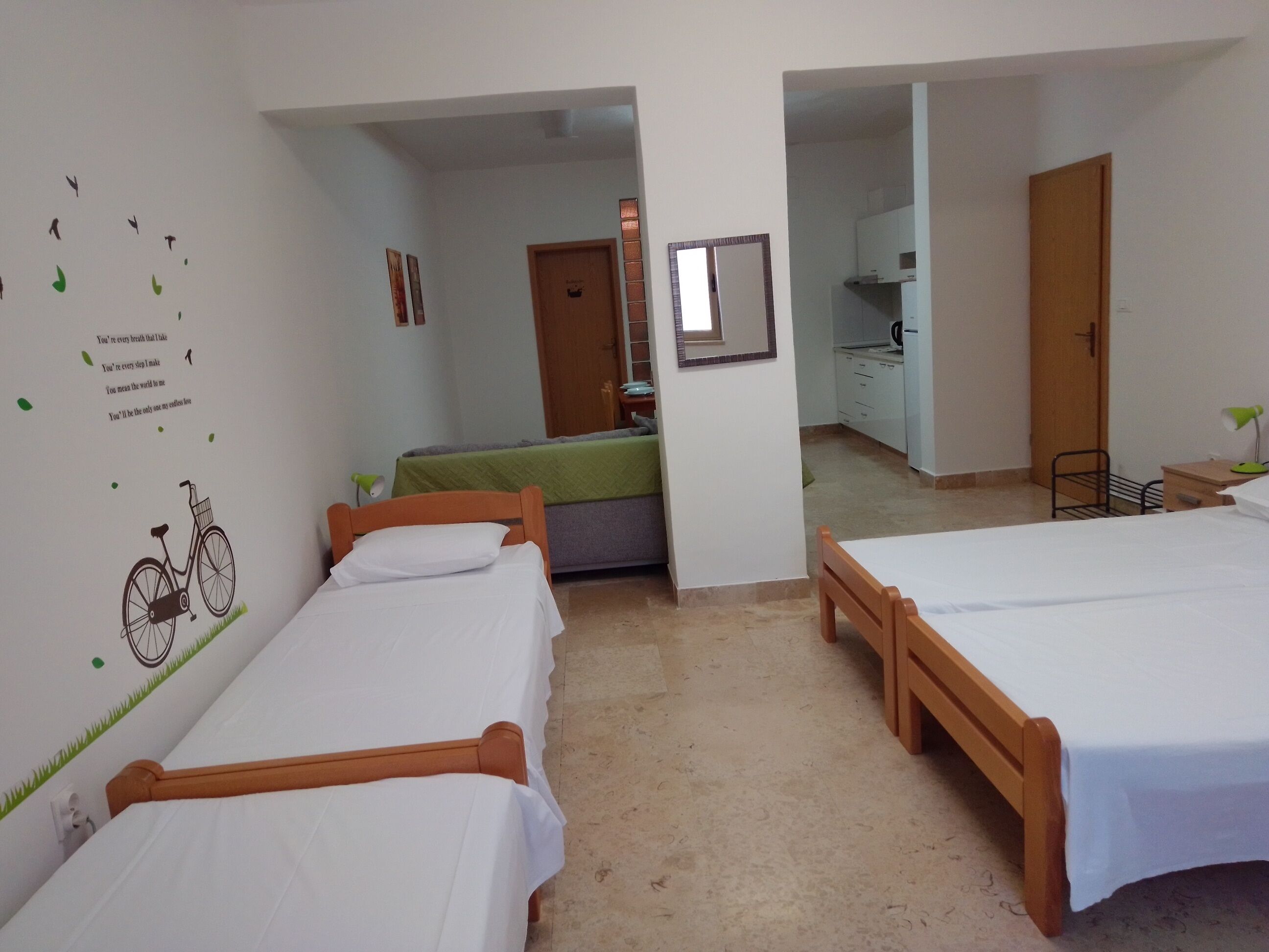 A hotel room with two single beds, a kitchenette, and a bathroom visible through an open door.