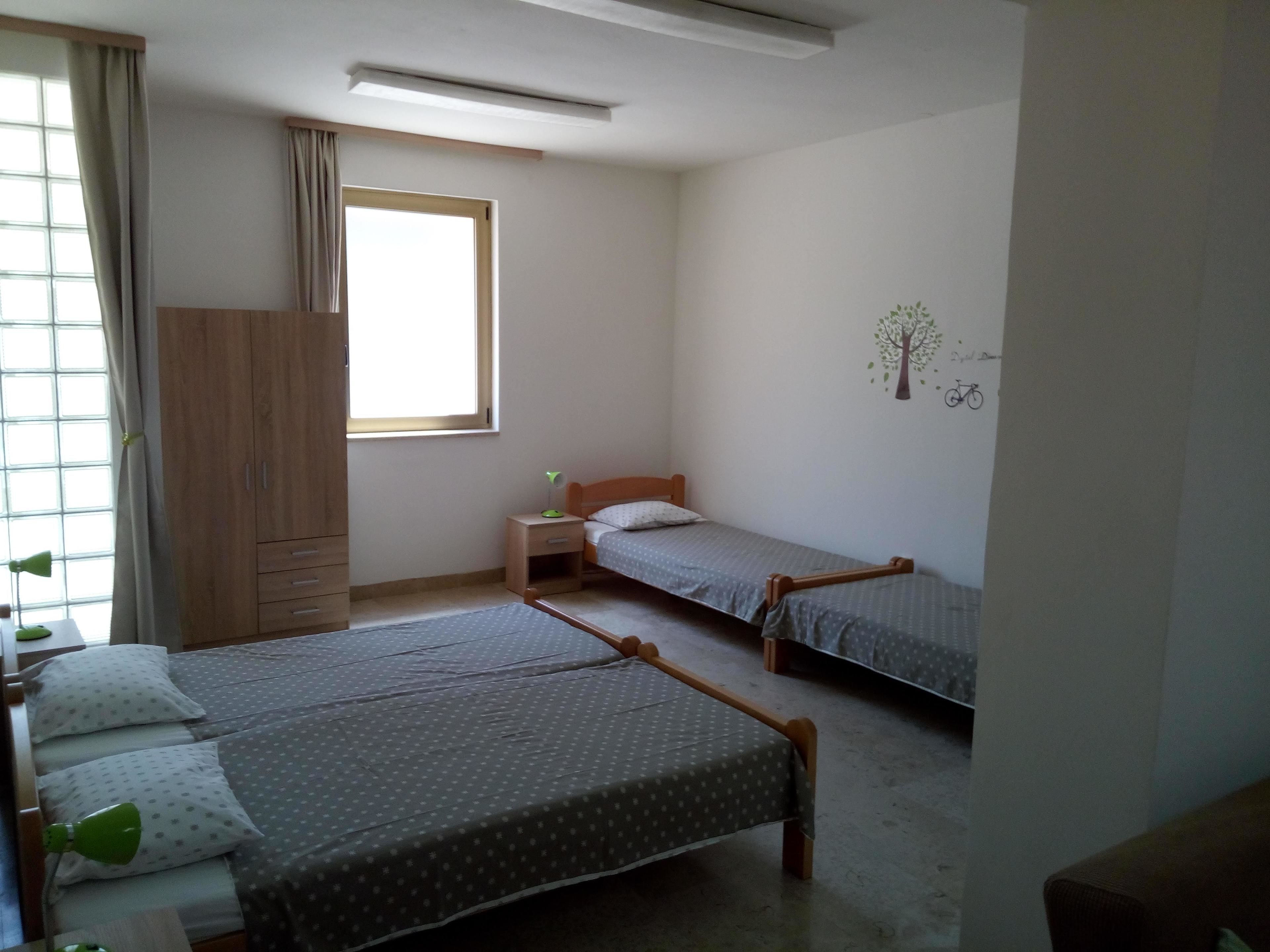 A bedroom with two single beds, a wardrobe, a window with curtains, and a wall decal.