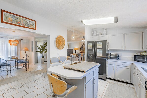 A modern kitchen with white cabinets, a central island, and a dining area with a table and chairs. - The Best Kept Secret on the Gulf =Newly Renovated 3BR St. Joe Beach House. (St Joe Beach)