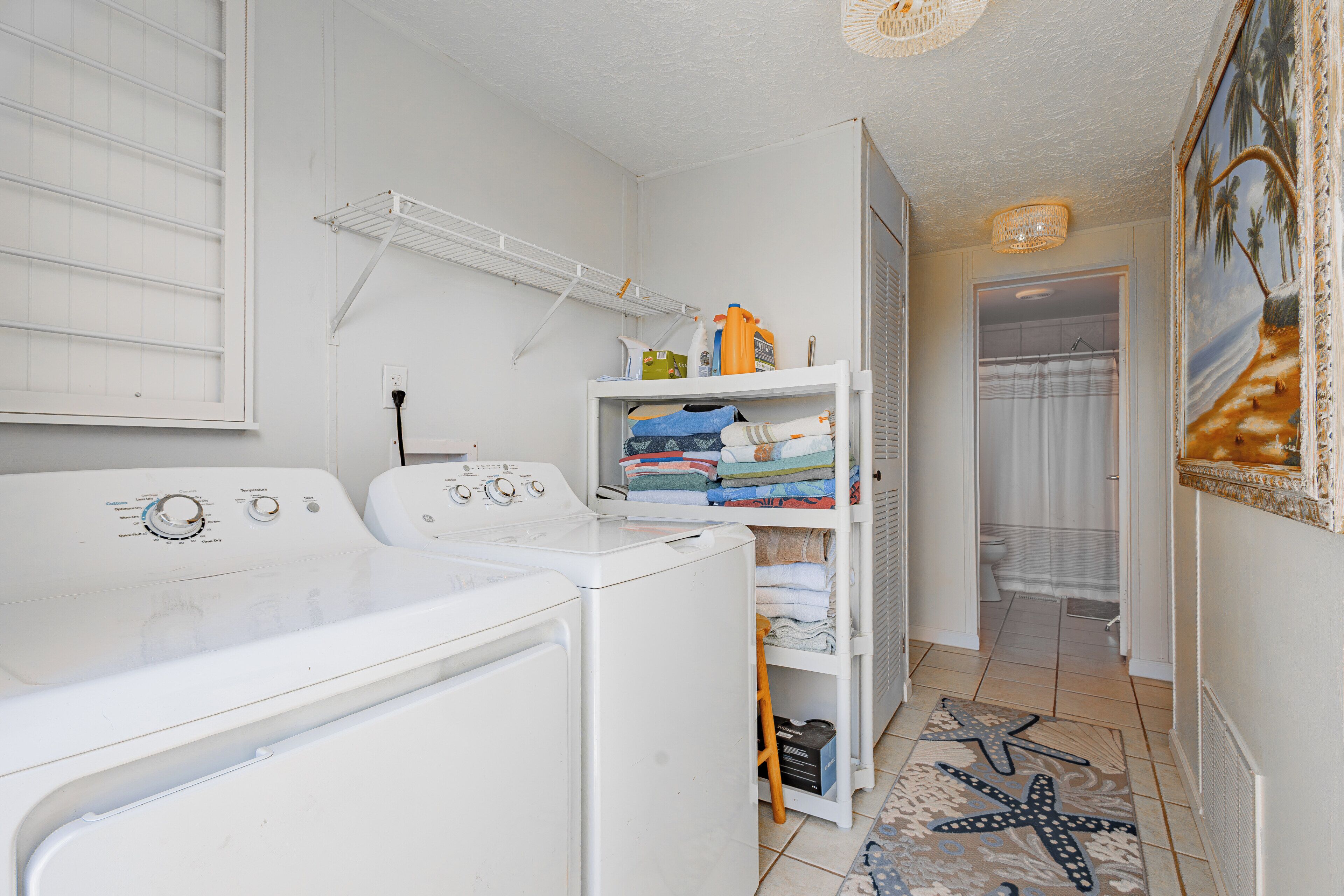 A laundry area with a washing machine, drying rack, and shelves with folded clothes.
