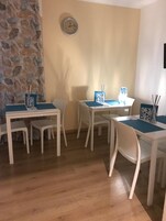 Un'area pranzo con tavoli e sedie bianche, un muro in pietra e un orologio a parete.