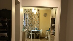 A narrow hallway leading to a dining area with a table and chairs, a clock on the wall, and a patterned curtain. - Papali (Catania)