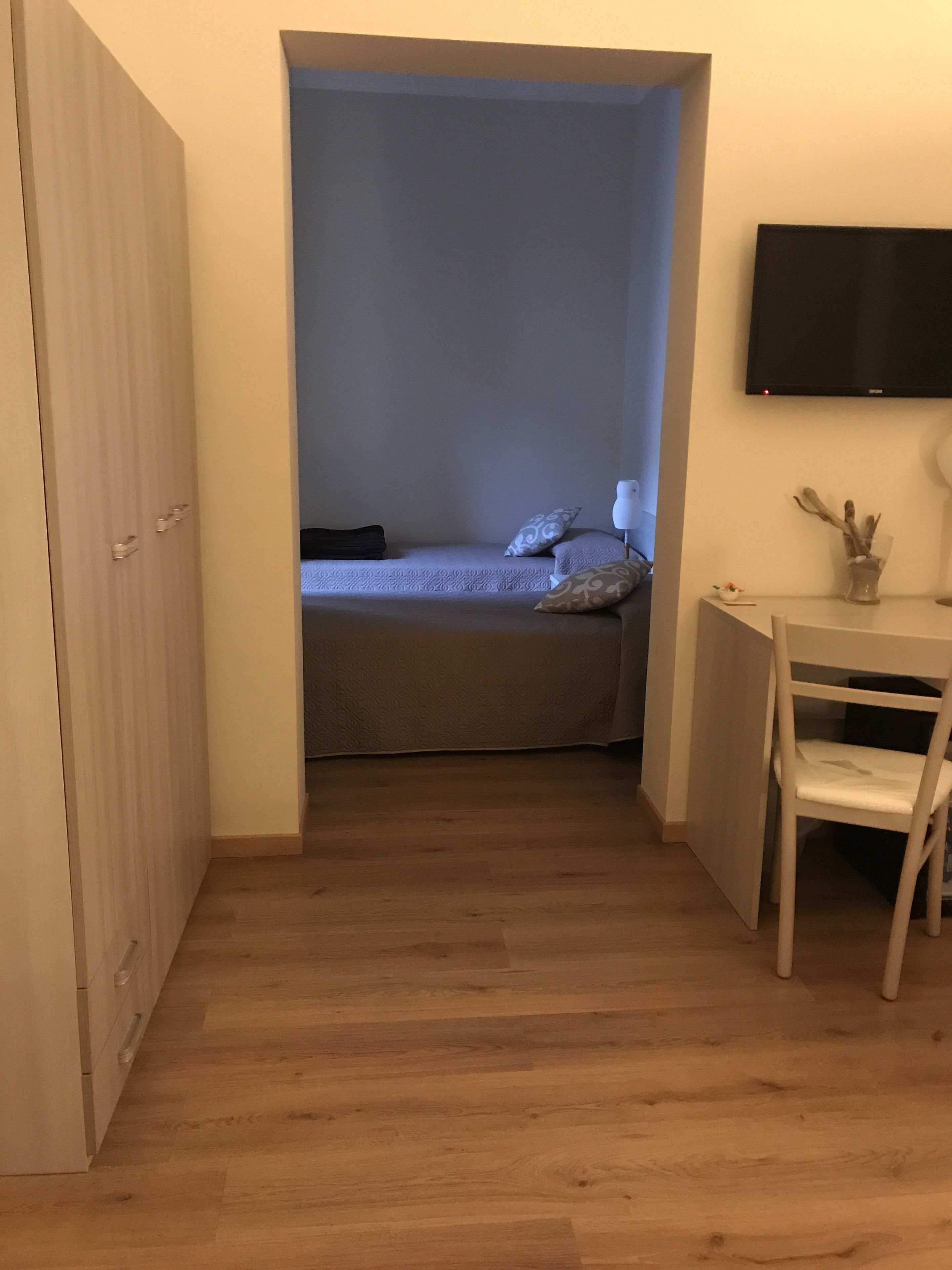 Ein kleiner, schmaler Raum mit einem Bett, einem Schreibtisch und einem an der Wand befestigten Fernseher.