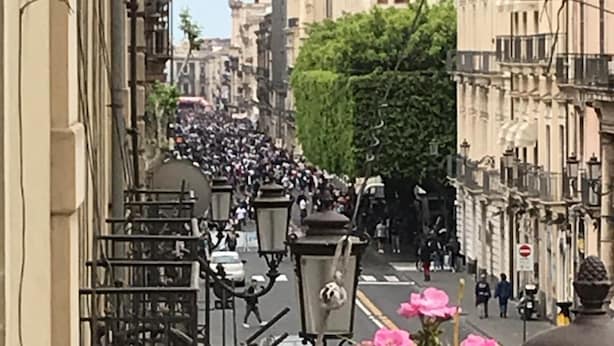 A street view with buildings, a crowd, and a street lamp. - Papali (Catania)
