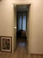 Un corridoio stretto che porta a una camera da letto, con un letto, un quadro appeso e una porta con tenda.