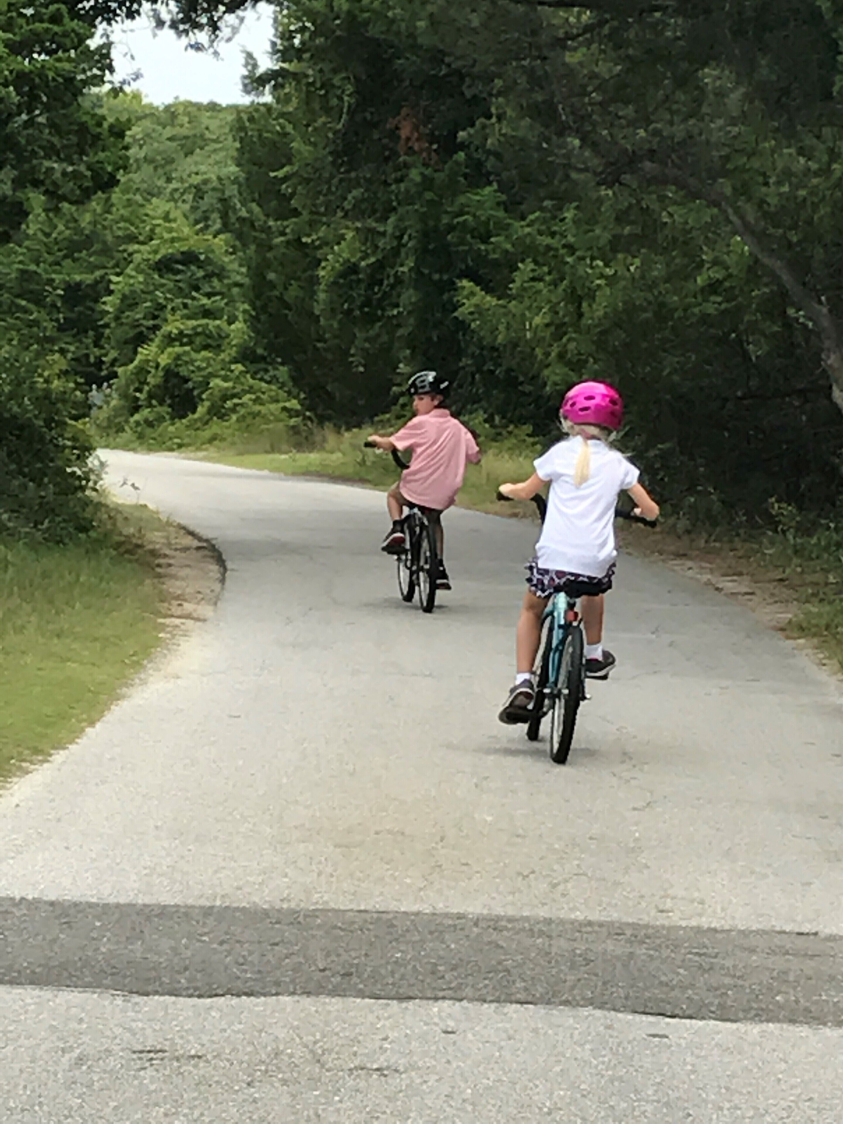 Dos niños montando bicicletas en un sendero pavimentado rodeado de vegetación.