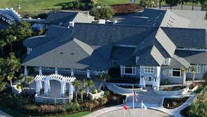 A large, modern house with a symmetrical roof design, multiple entry points, and a well-maintained lawn.