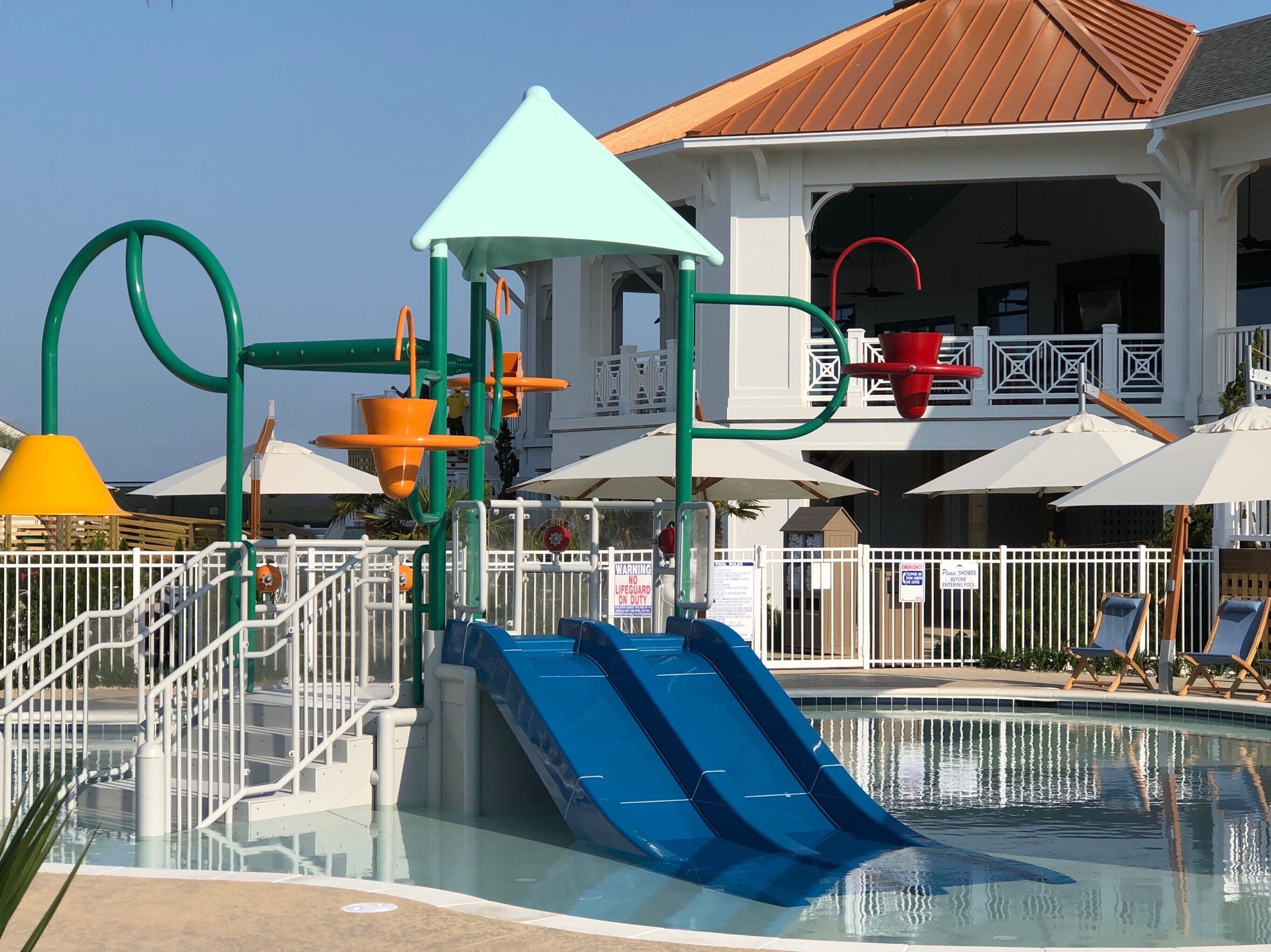A pool area with a blue slide, a play structure, and umbrellas.