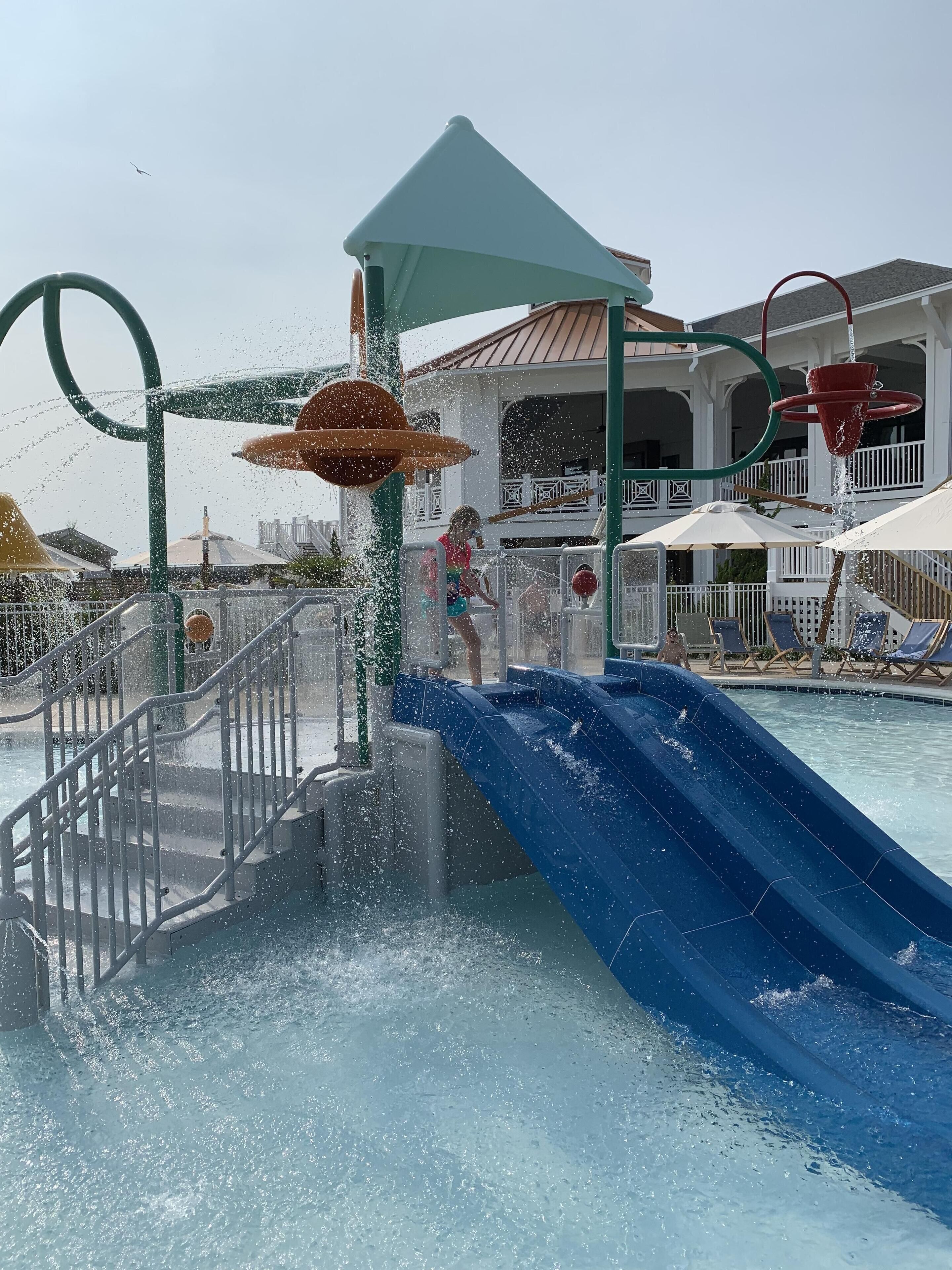 A water park with a blue slide, a water fountain, and a pool area with lounge chairs.
