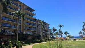 A multi-story hotel with balconies, a well-maintained lawn, and palm trees. - Ocean View Upgraded Top Fl HOKU711 Shaded Lanai see condo comparison chart  (Lahaina)