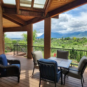 A covered outdoor seating area with a table and chairs, overlooking a mountainous landscape. - Colorado Springs Mesa Retreat (Colorado Springs)