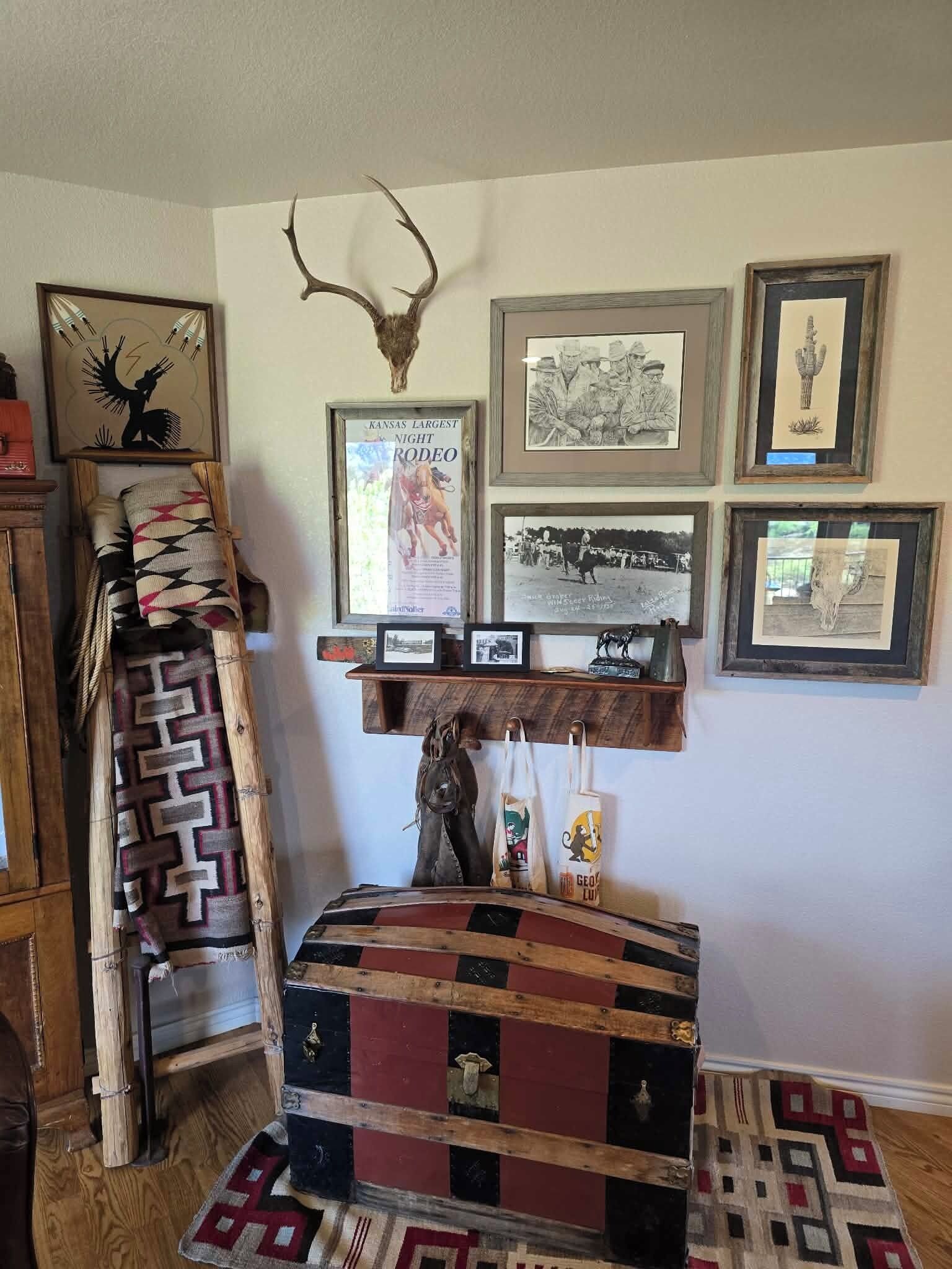 A room with a wooden chest, a mounted deer head, framed artwork, and a patterned rug.