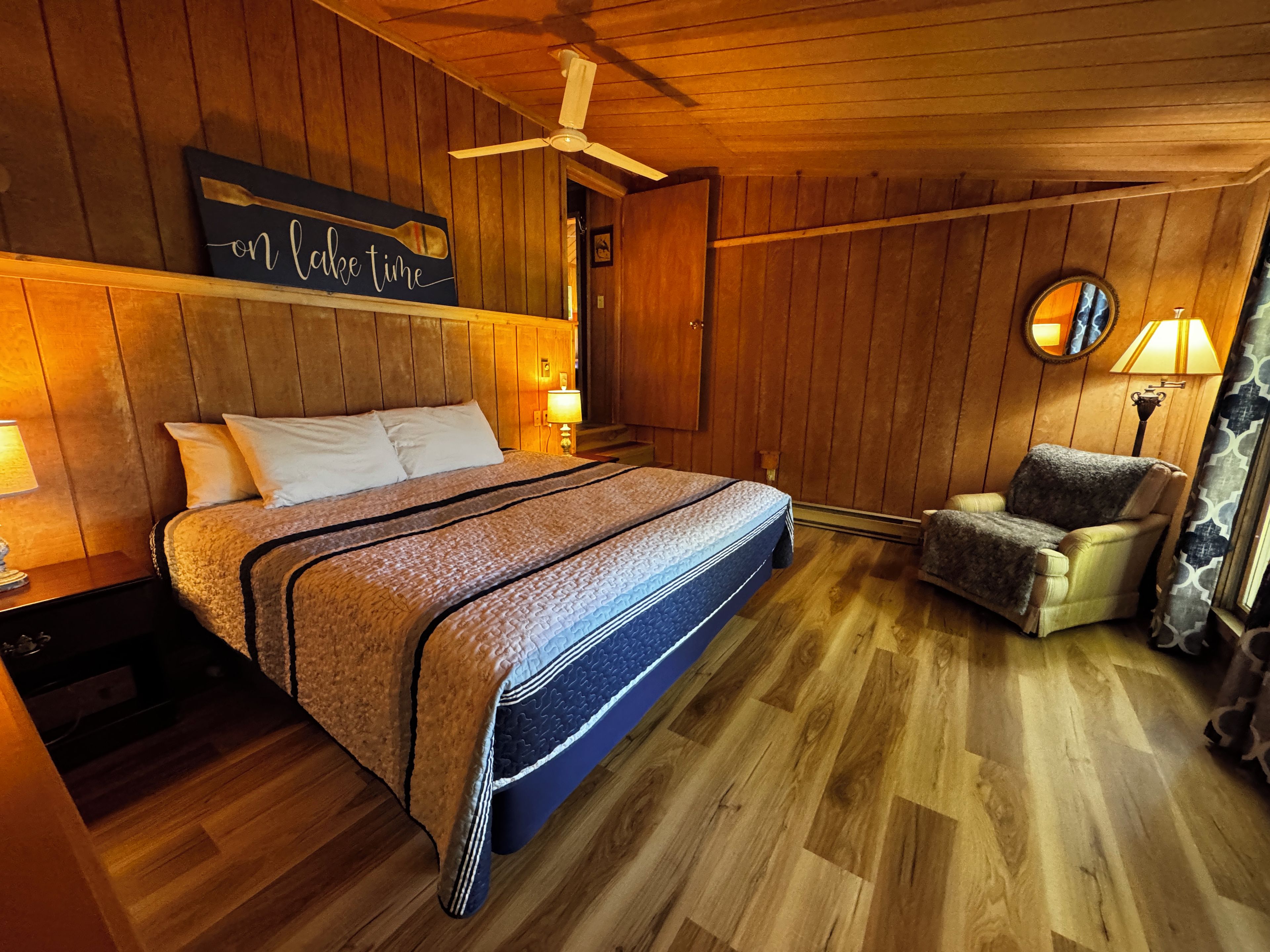 Ein Zimmer mit Holzvertäfelung, einem Bett, einem Sessel, einem Deckenventilator und einem an der Wand befestigten Schild.