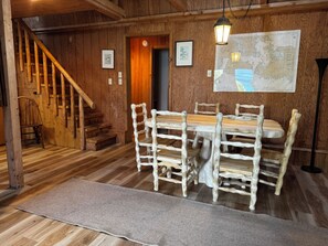 A wooden interior with a dining table, chairs, a staircase, and a map on the wall.