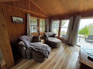 A cozy cabin interior with wooden walls, a sofa, a table, and a view of the outdoors.